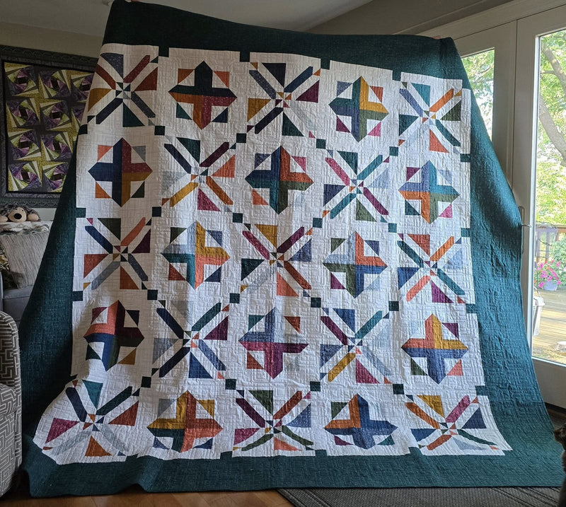 A finished, quilted star-pattern quilt held up in a living room