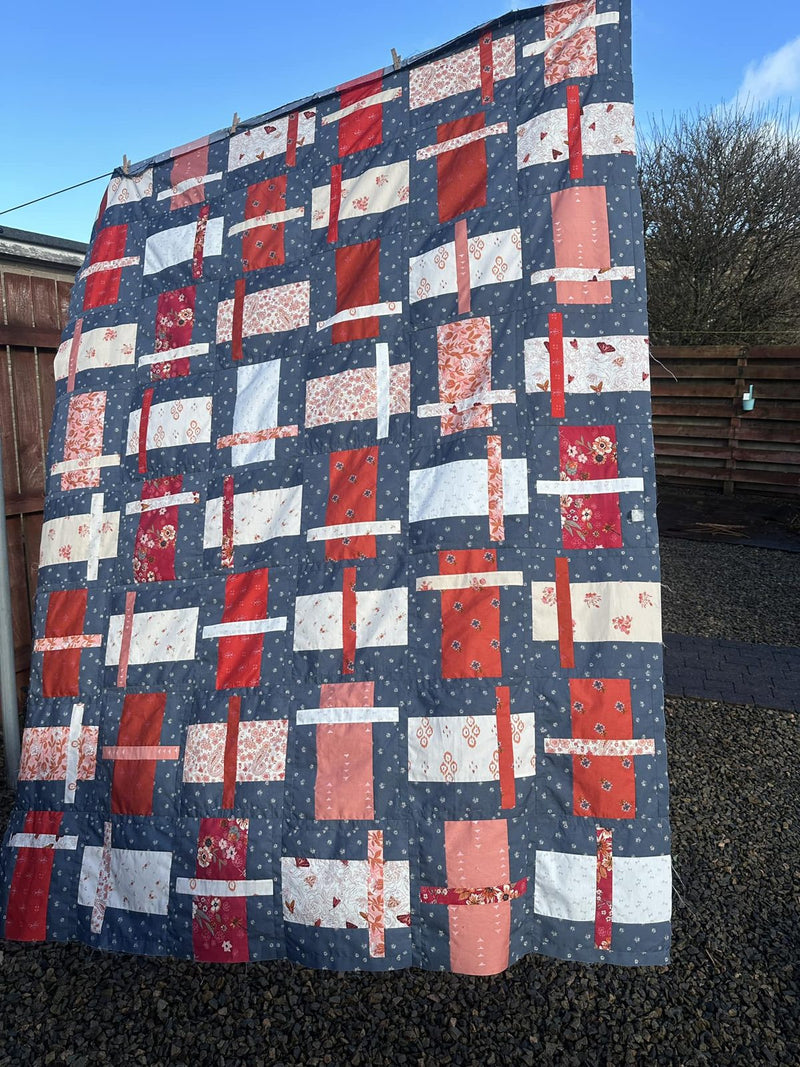 A finished quilt top hanging on a clothesline under a blue sky