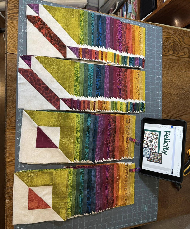Rainbow strip sets on a cutting mat, with the pattern on an iPad